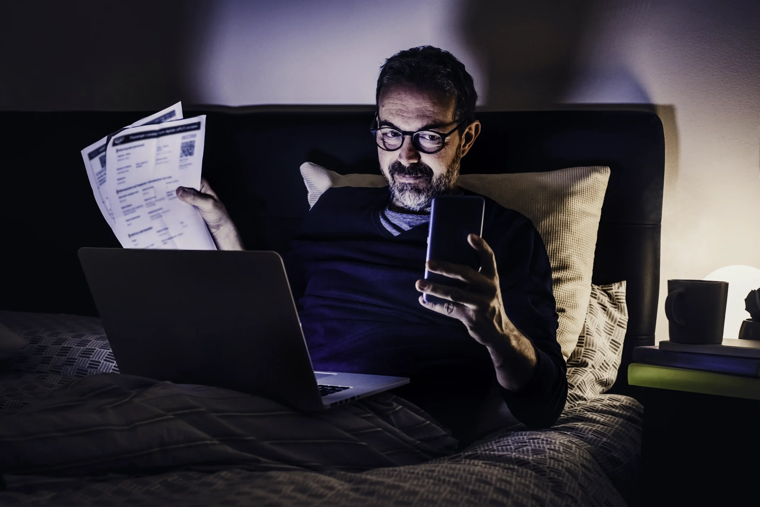 man keeps electric bill laying on bed and lokss at the phone